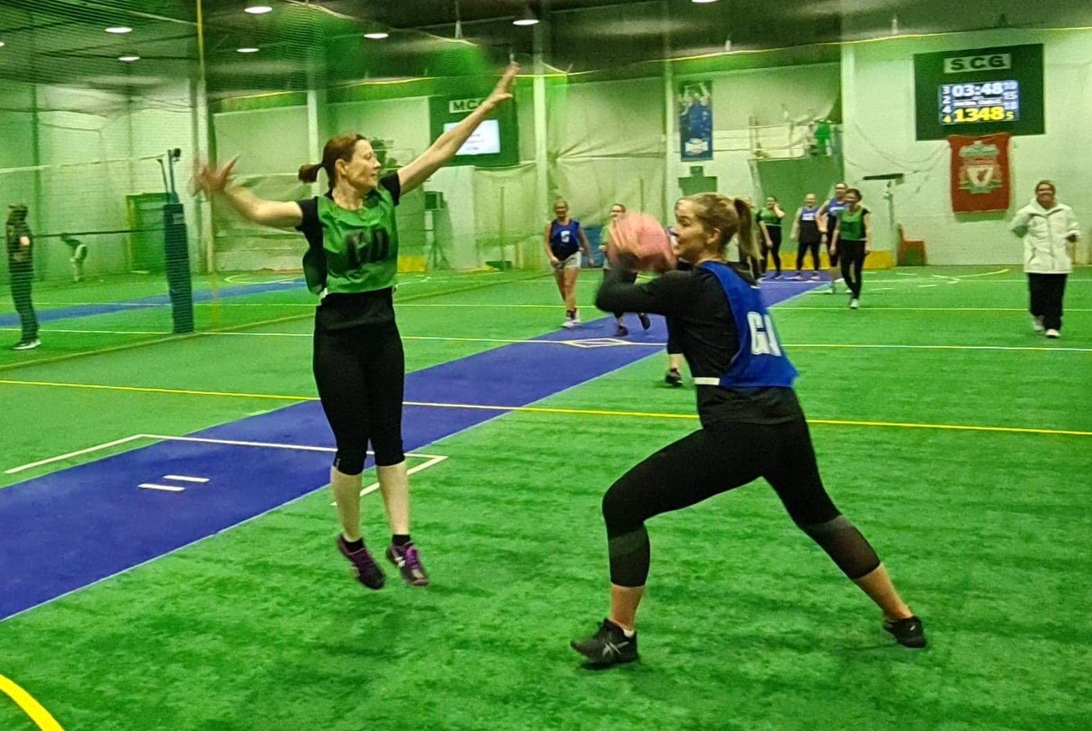 2 netball players playing indoors. 1 jumping 1 throwing