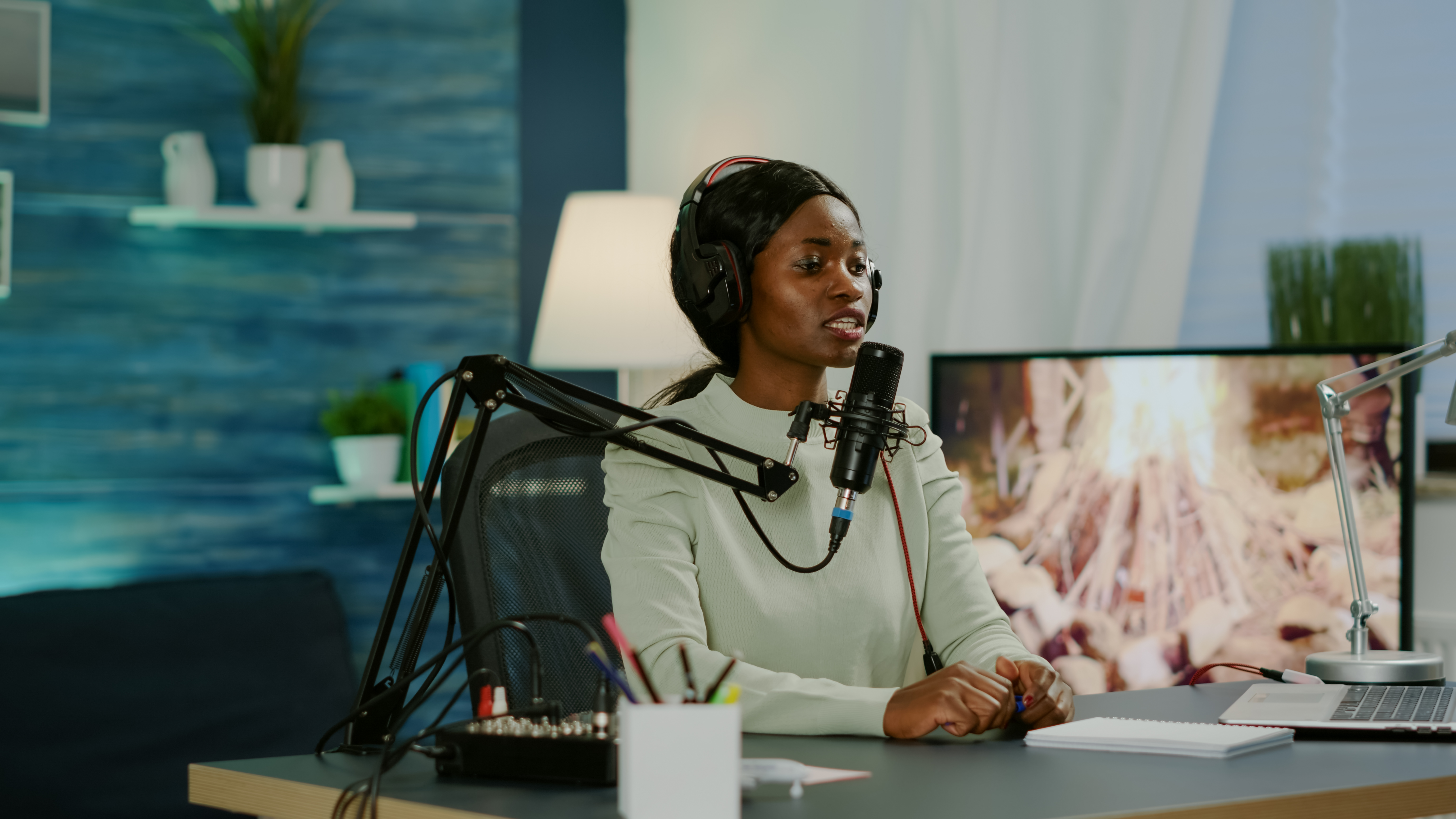 Black woman podcast host wearing headphones, talking into microphone