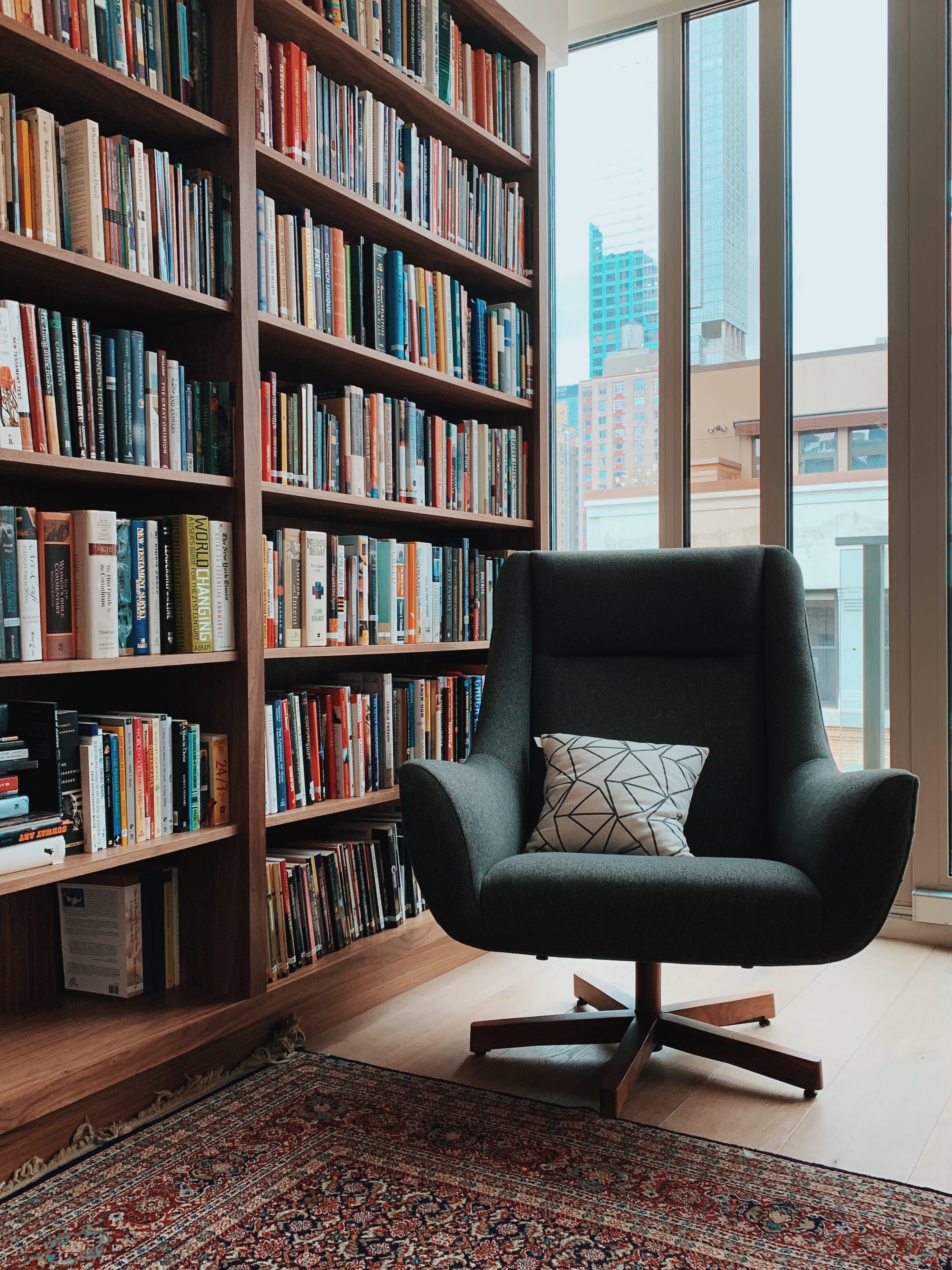 Ceiling-high bookshelf with a cozy black chair and window.