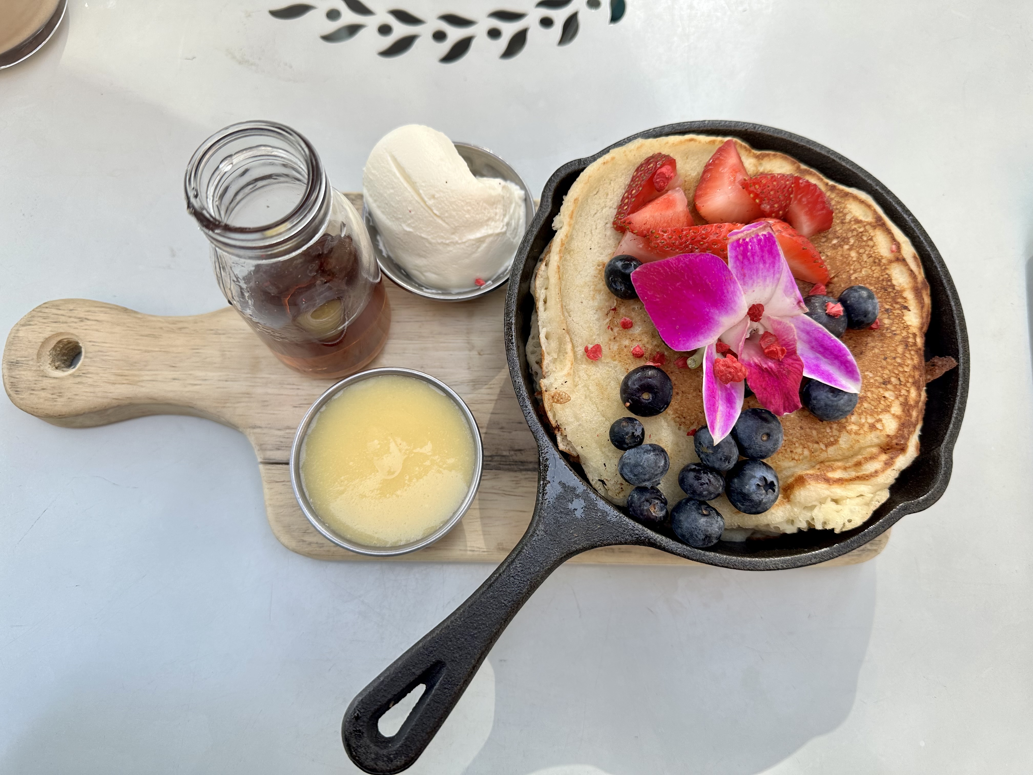 Pancakes in a skillet topping with pink flower and berries