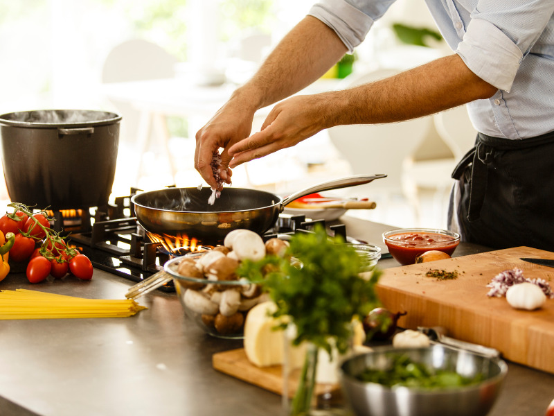 A man's arms shown cooking over a stove