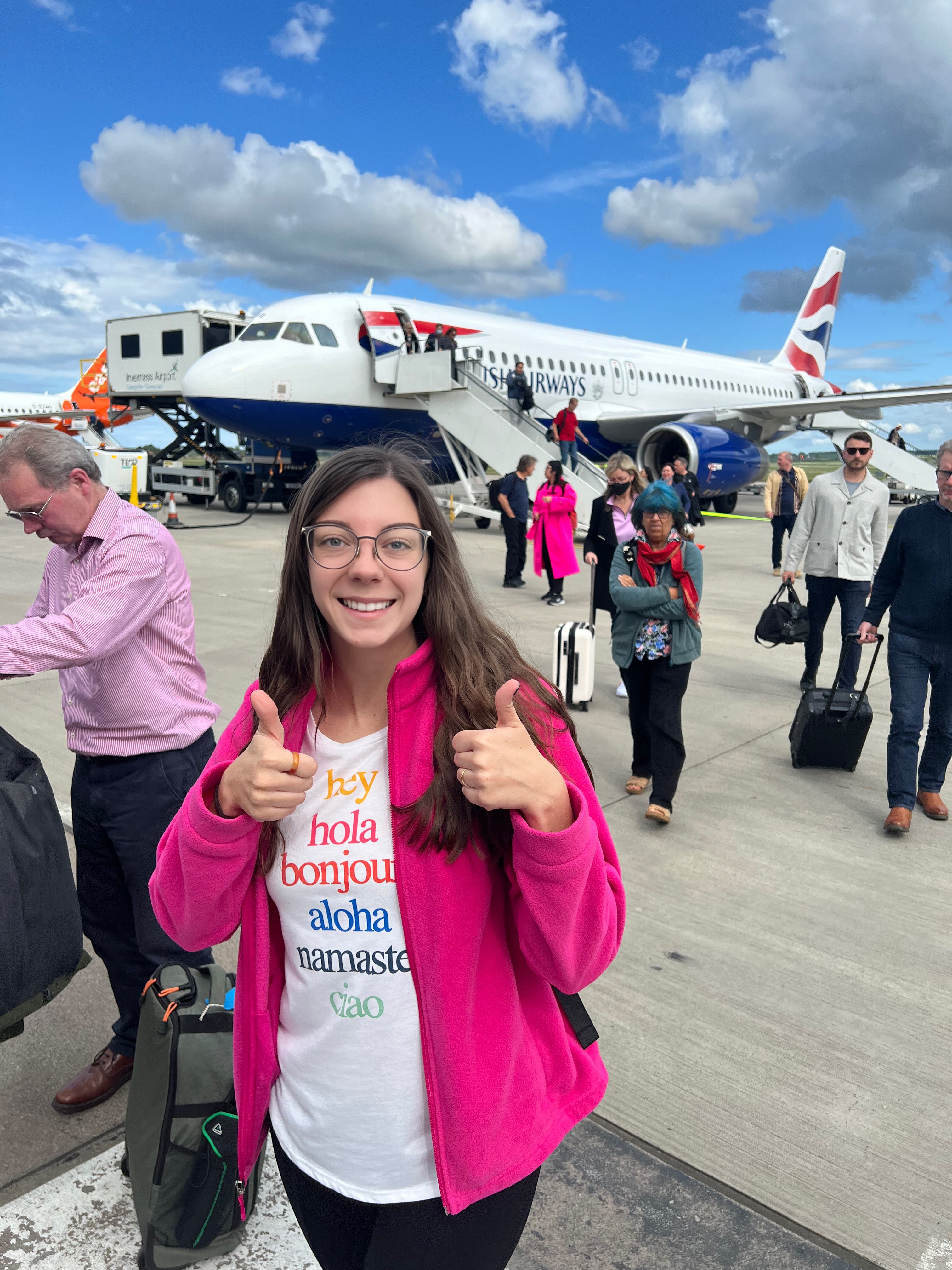 girl with two thumbs up standing infront of a British Airways plane