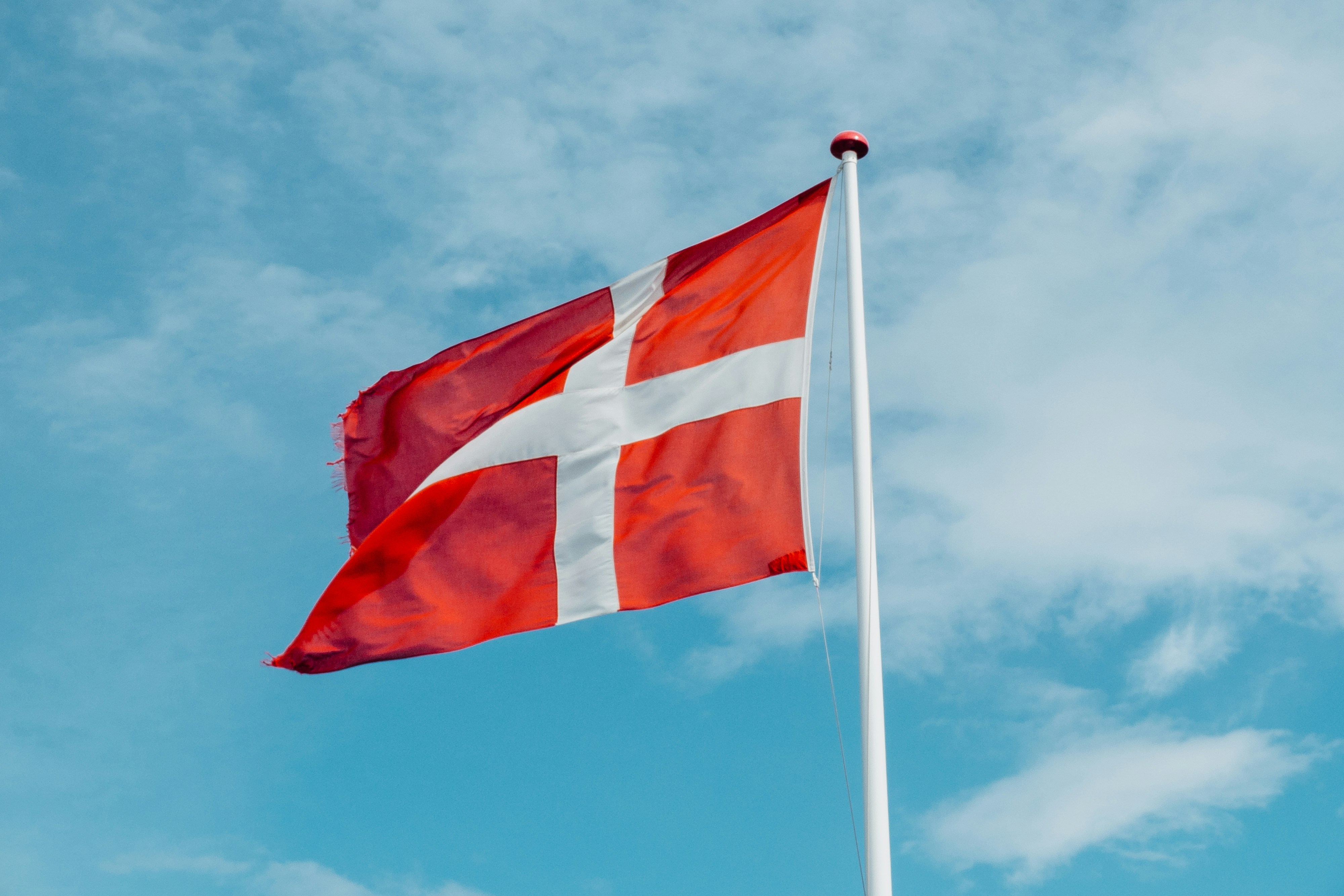 danish flag flying high with backdrop of blue sky and small clouds