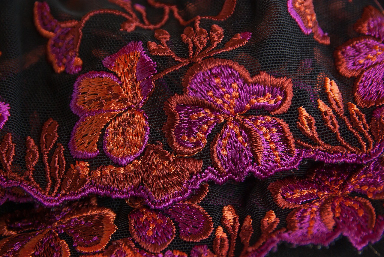 a close-up of embroided lace in botantical inspired pattern in vibrant pinks and oranges.