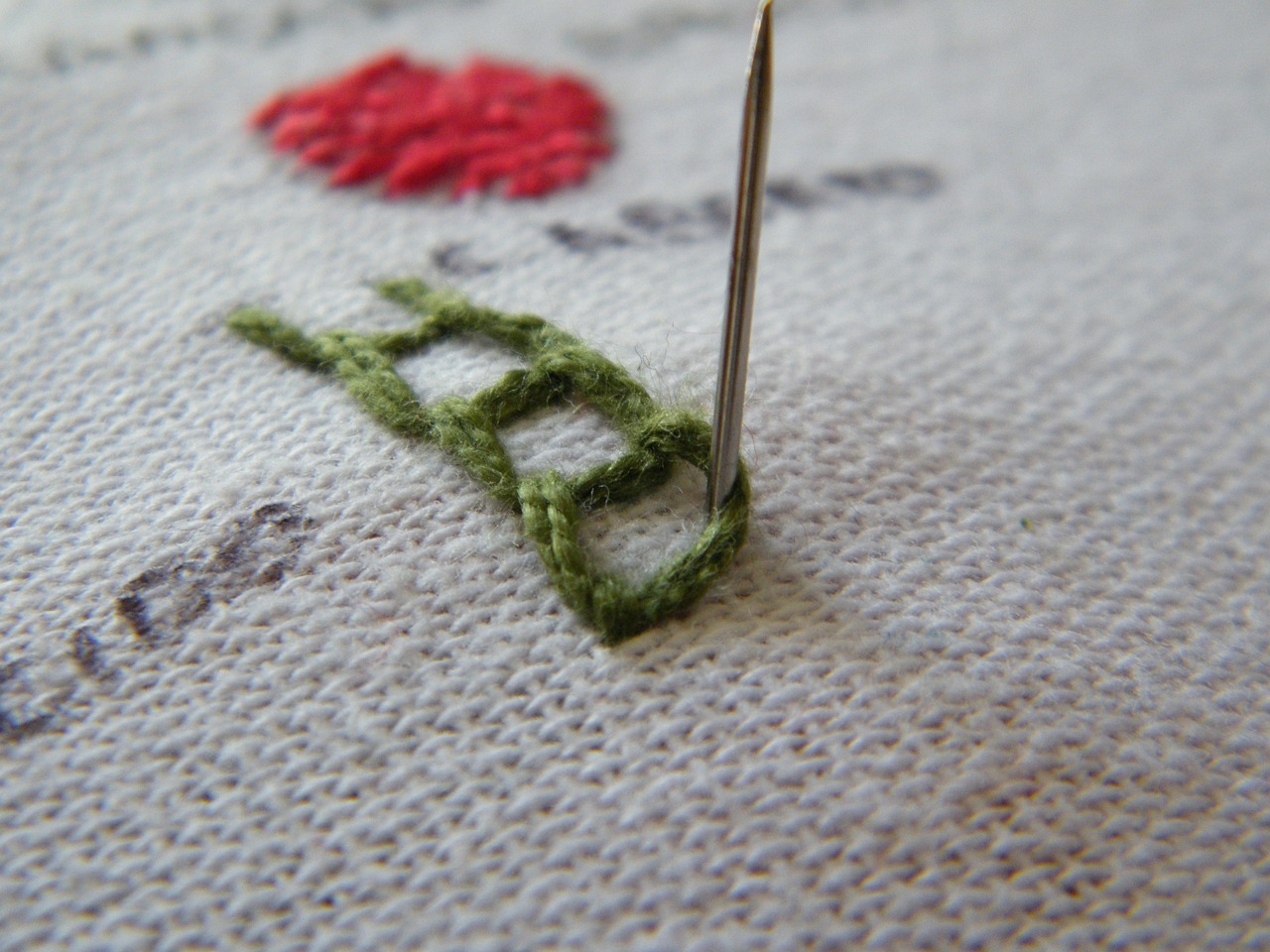 canvas close-up with a pattern being added mid stitch with a green thread.