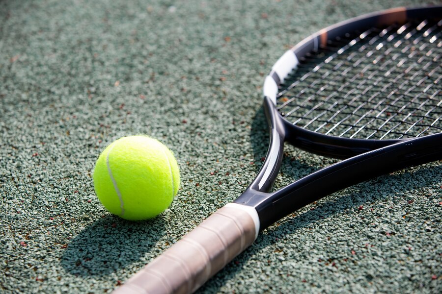 Close up of tennis racket and ball on a dark green hard court