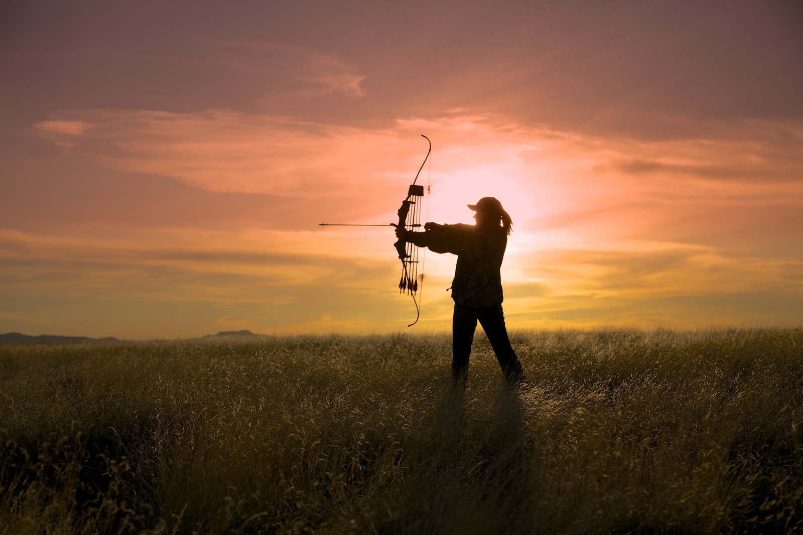 Woman drawing her bow silhouetted against the sunrise.