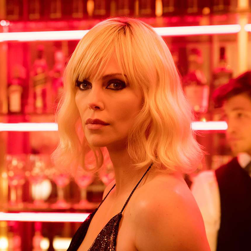 Charlize Theron as Lorraine Broughton wearing a sleek, backless dress. She has, appropriately for a film titled Atomic Blonde, blonde hair.