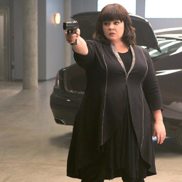 Melissa McCarthy as Susan Cooper holding a gun, stood by a parked car