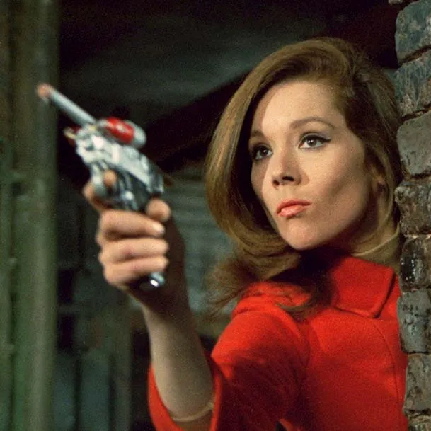 Diana Rigg as Emma Peel, dressed in red and holding a gun