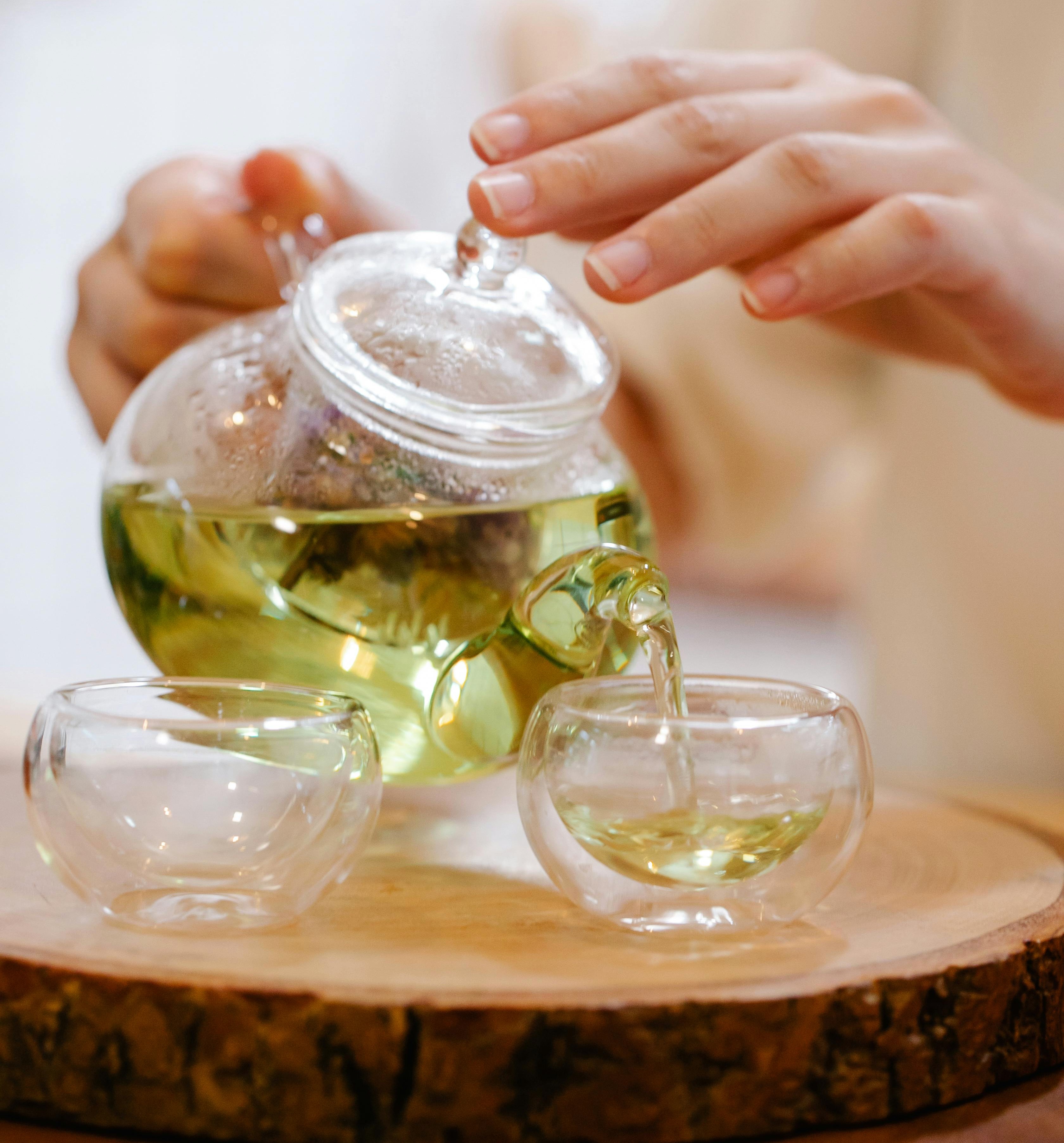 A cup of green tea is being poured from a kettle
