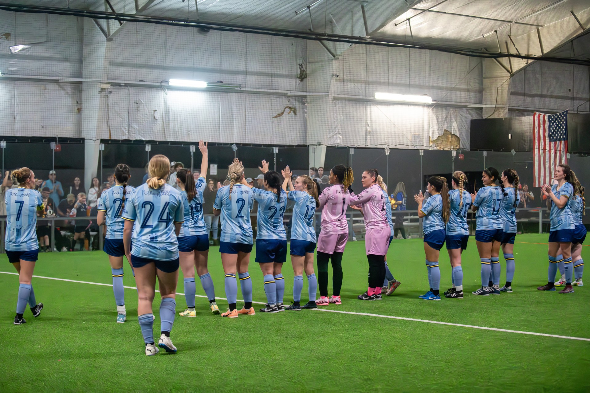 Team on indoor soccer field waving at the crowd.