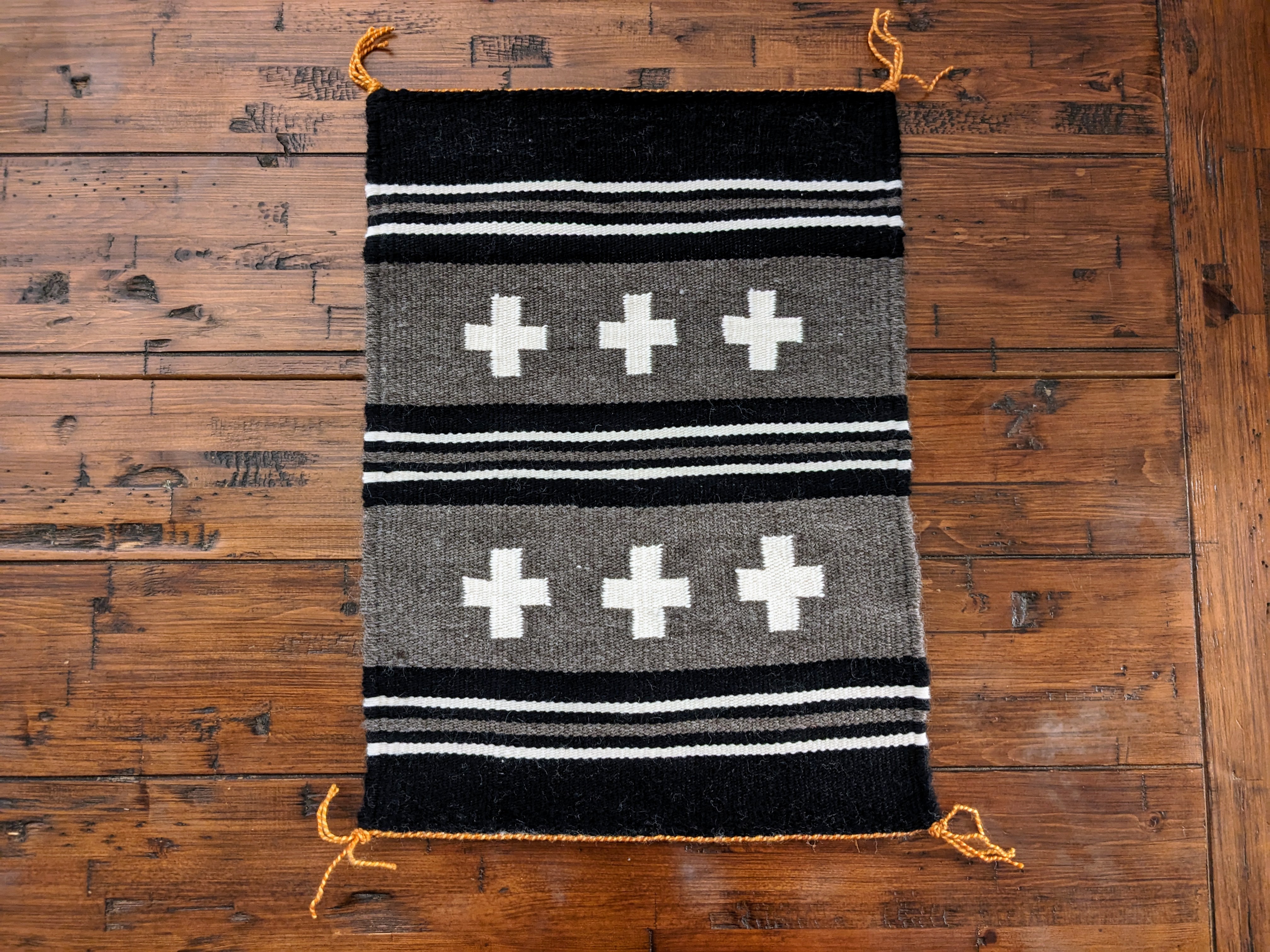 Black, gray, and white Navajo rug laying on a wooden table, artist is myself