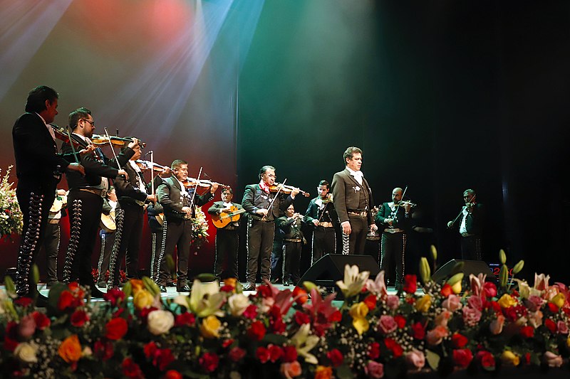 Group of musicians in traditional mariachi costumes playing music on stage.
