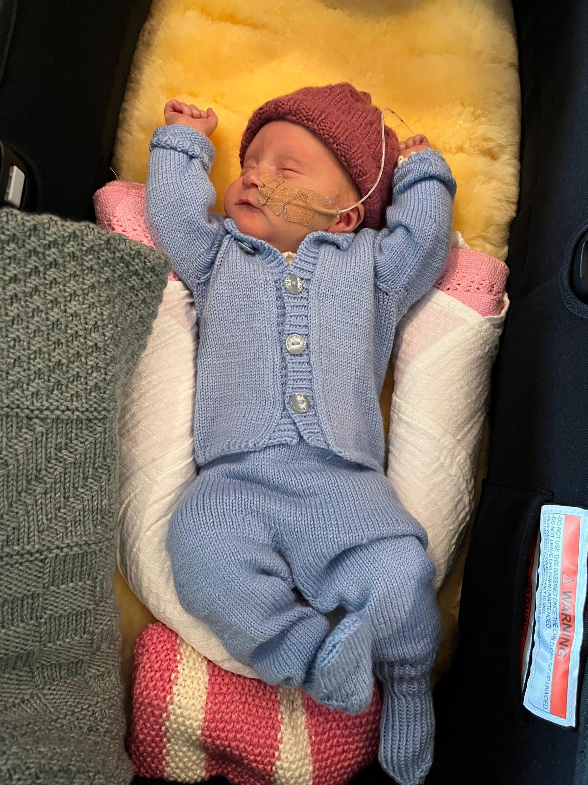 Premature baby in blue knitted jacket and pants
