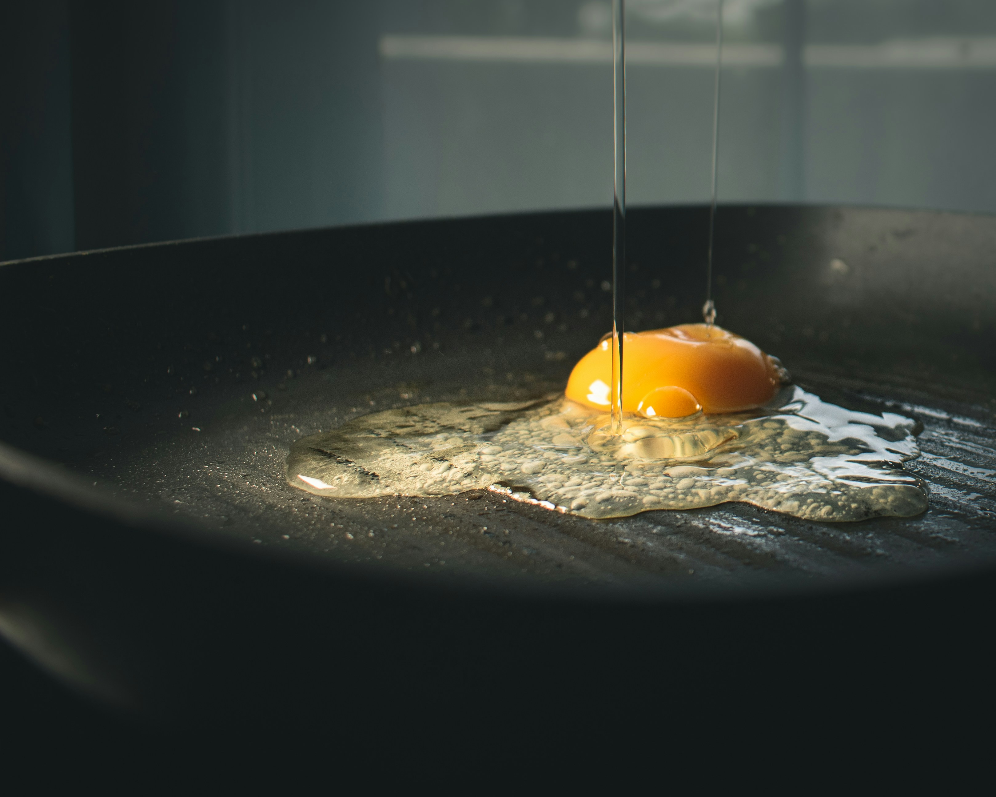 an egg being dropped on hot cast iron skillet