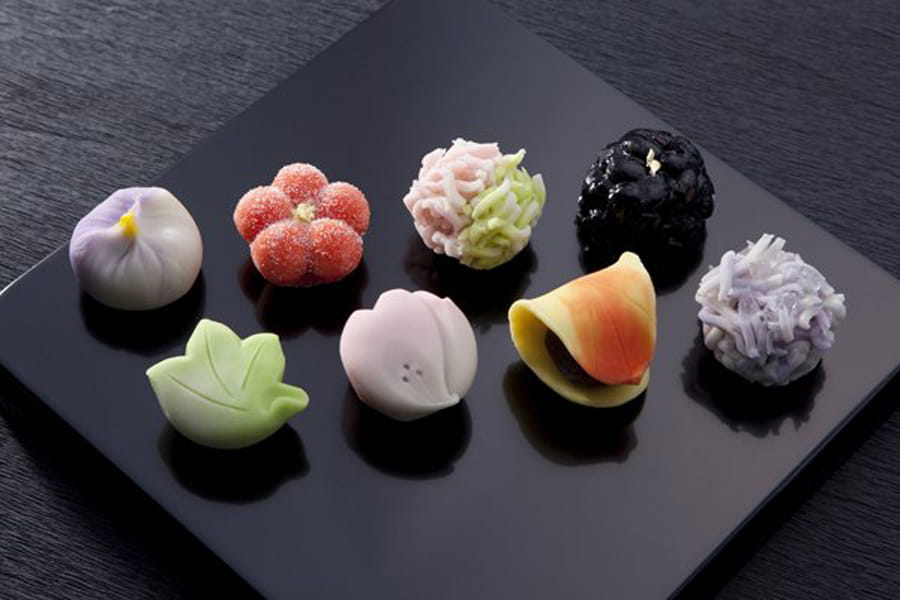 Wagashi of different types and colors on a black plate.