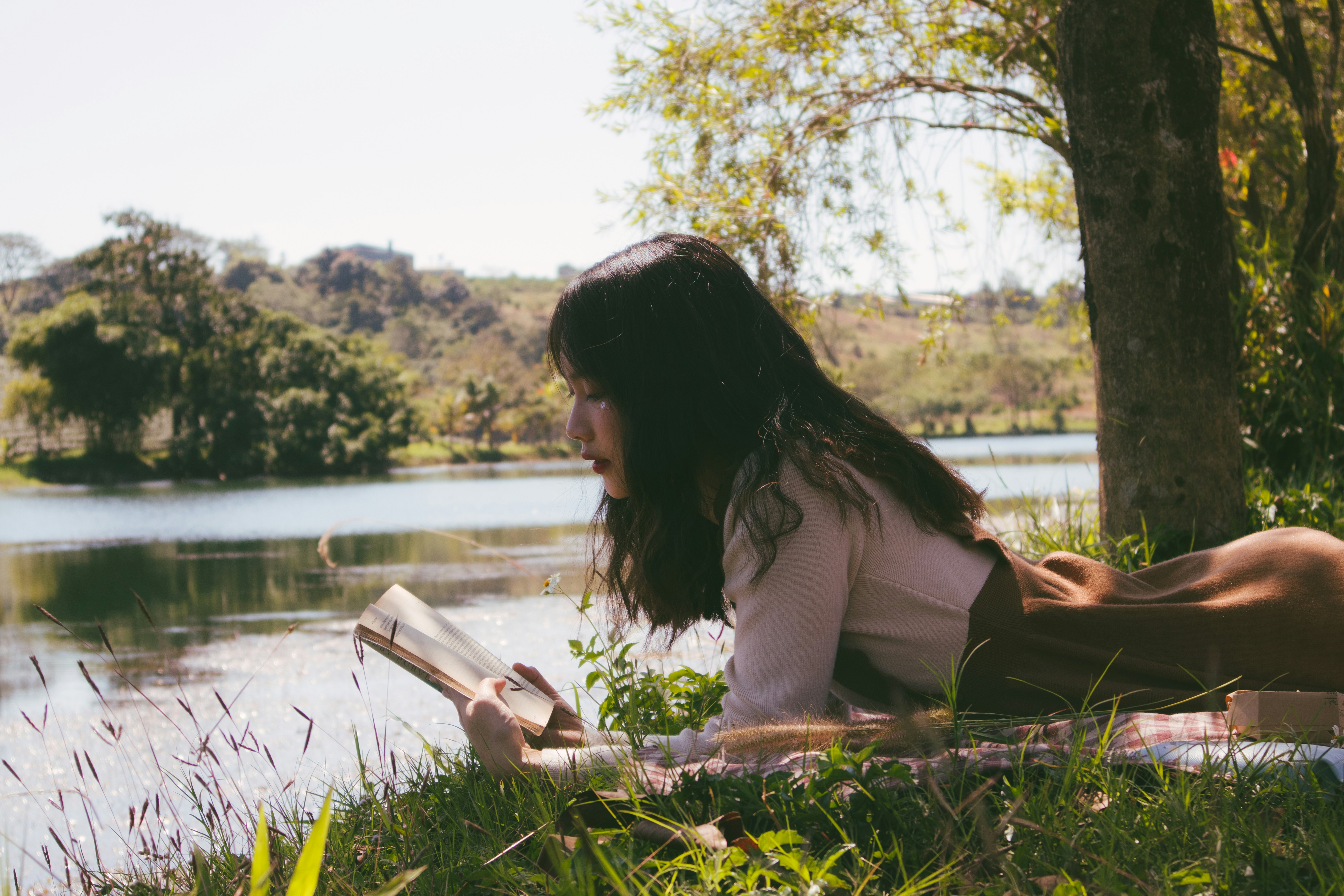 girl reading in the grass by a river