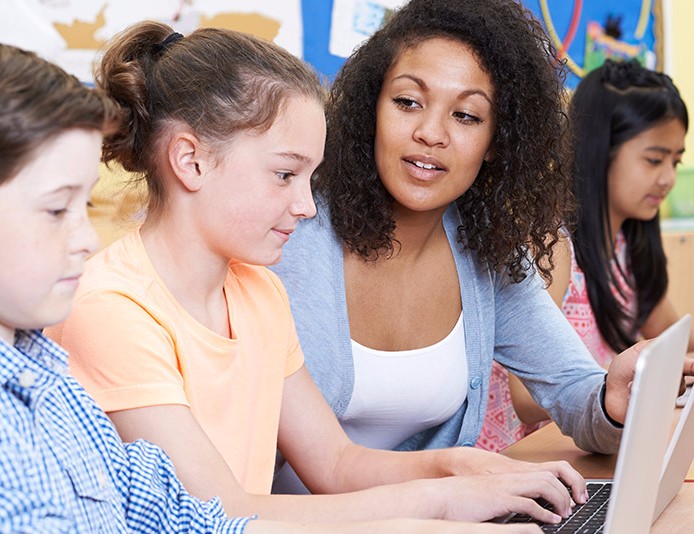 african-american female teacher helping diverse group of young students at computers
