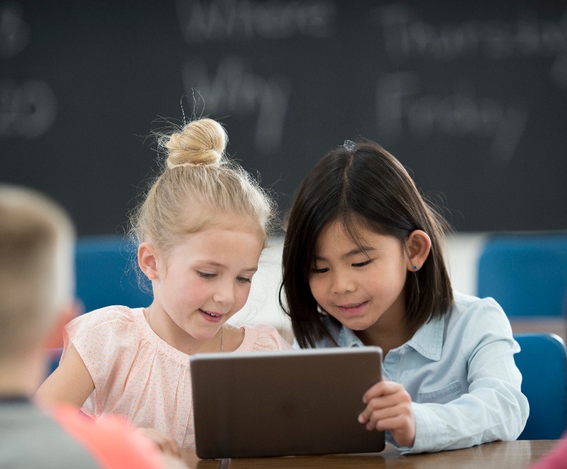 photo: young blonde girl staring intently at computer; fingers poised over keyboard; child making funny face in background