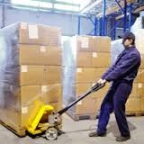 A stock handler at a grocery warehouse facility transfers pallets stacked with