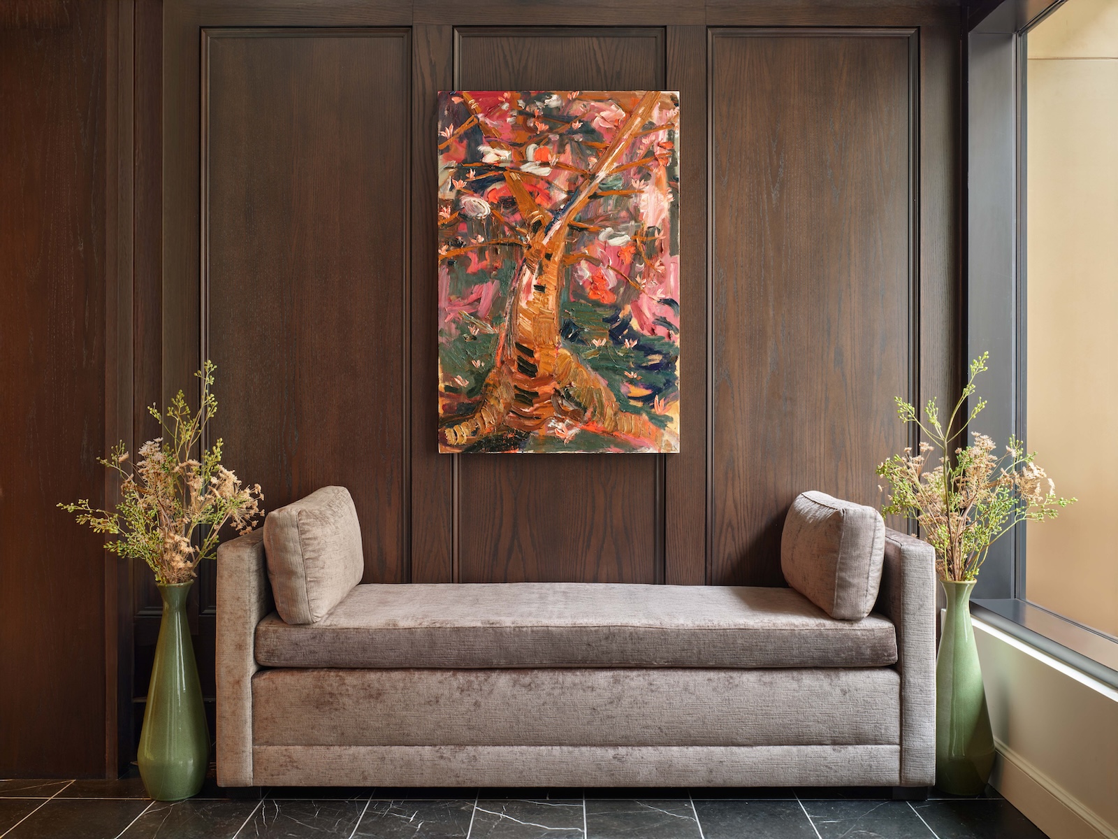 A lobby with a gray sofa, a colorful abstract painting, and two green vases with flowers.