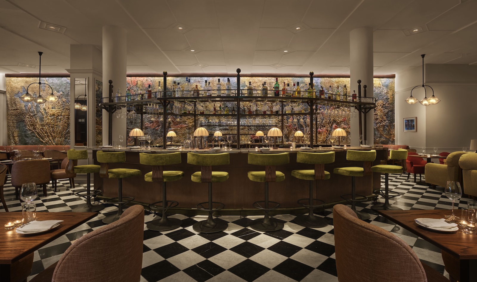 A wide view of a bar with green stools, a black and white checkered floor, and tables with chairs.