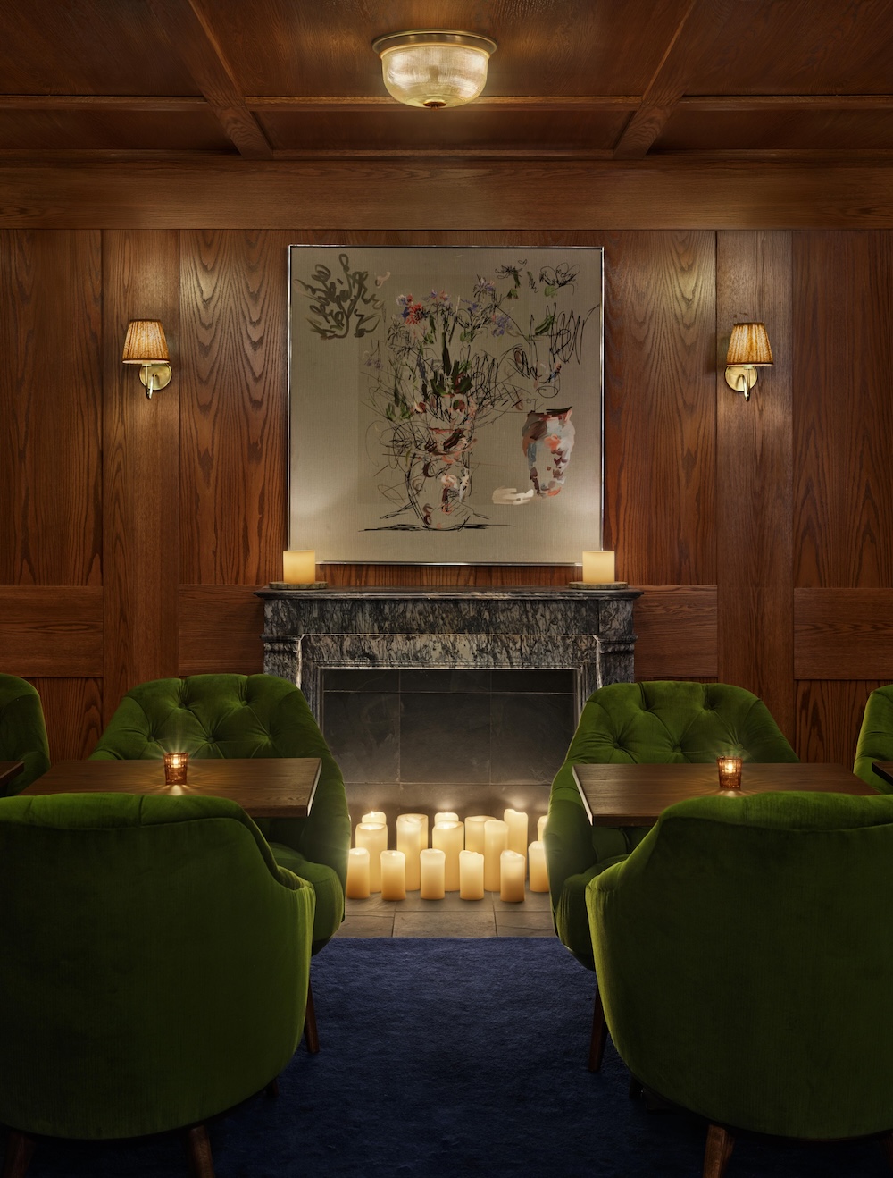 A cozy lounge with green chairs, a fireplace, and artwork on the wall.