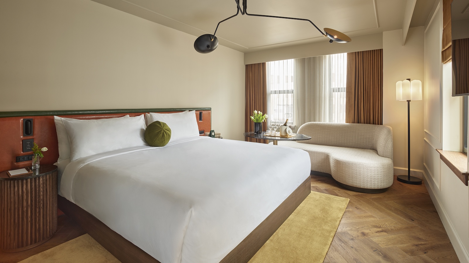 A hotel room with a large bed, a sofa, a lamp, and a window.