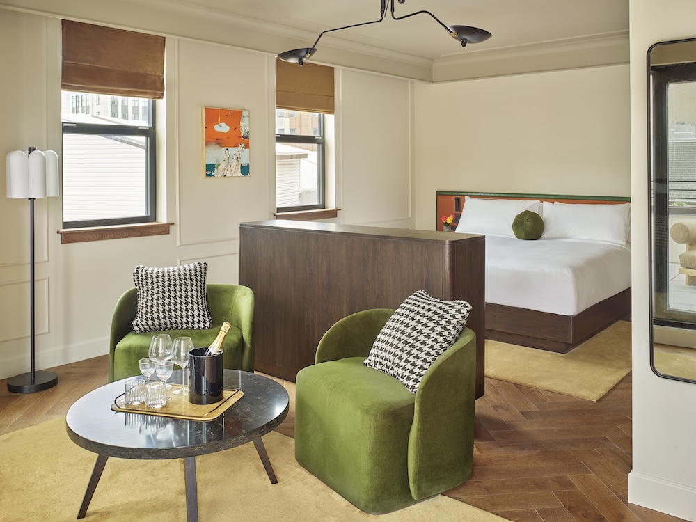 A luxurious hotel room with a king-sized bed, two green chairs, and a round table.