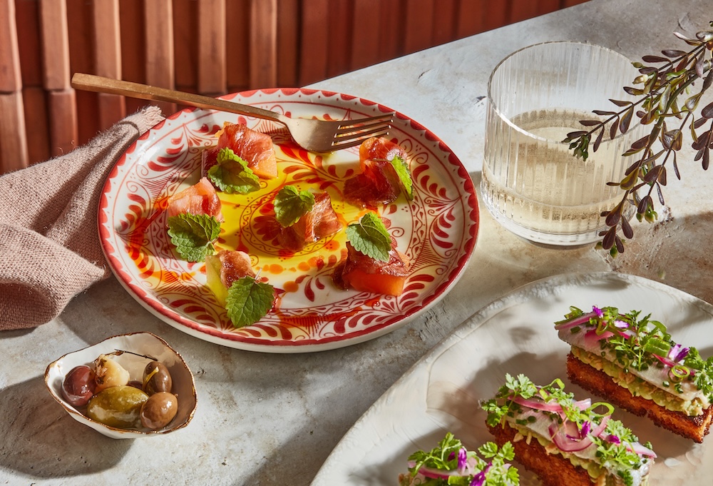 a plated meal on a table with a fork, glass of water, and olives