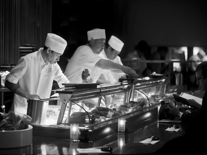 Three chefs in white uniforms prepare food at a counter.