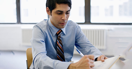 man at desk writing in notepad