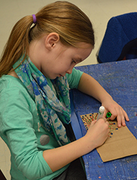 Second-grader Brynn Marshall colors a design on a paper bag