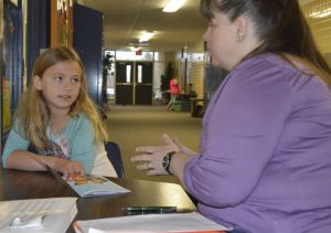 Central Elementary parent volunteer Stephanie Lapinski discusses a book with second-grader Eloise Tompkins; crowded classrooms force such tutoring into the hallway