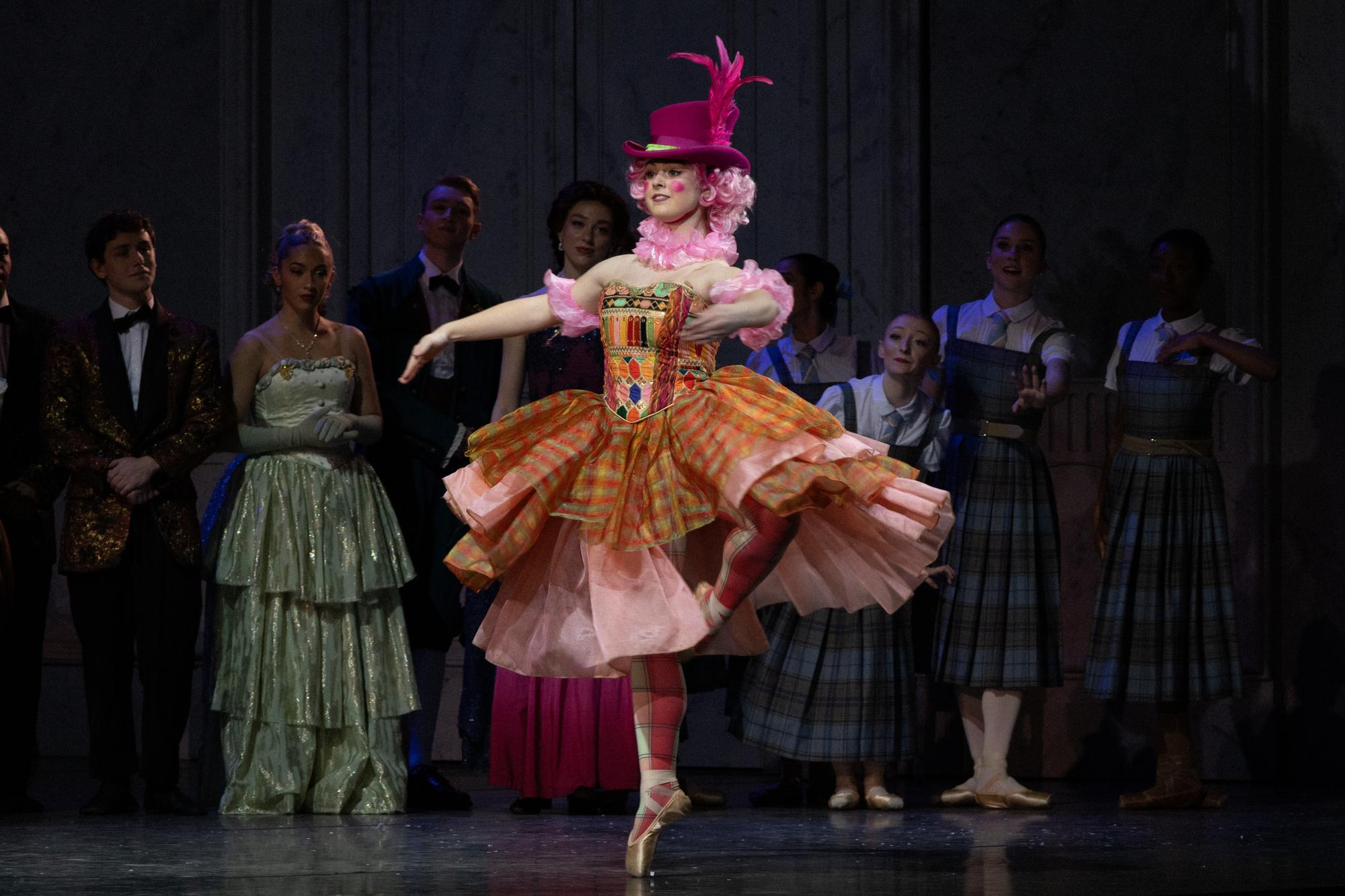 A dancer styled like a patchwork doll in a pink hat.