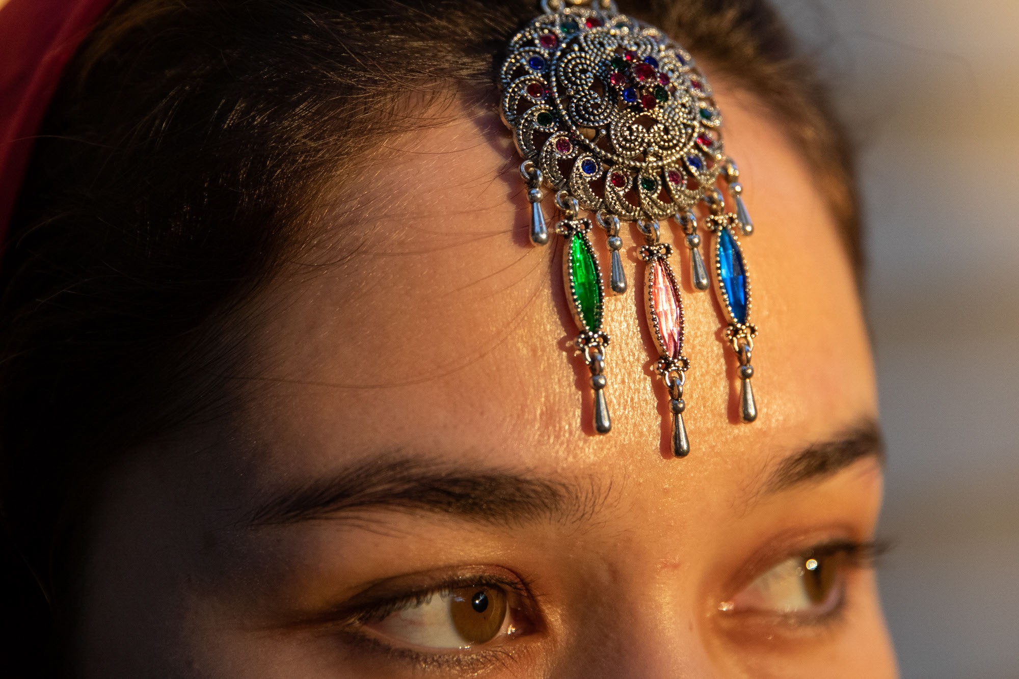  A woman wears a headpiece made of silver with colorful gems.