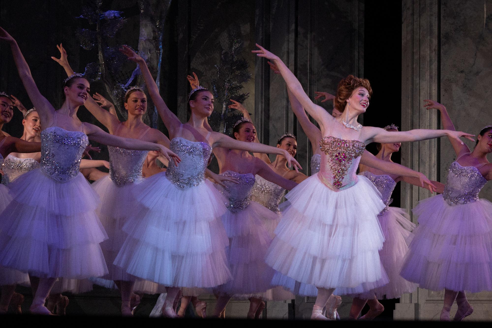 Dancers in white dresses make a synchronized motion.