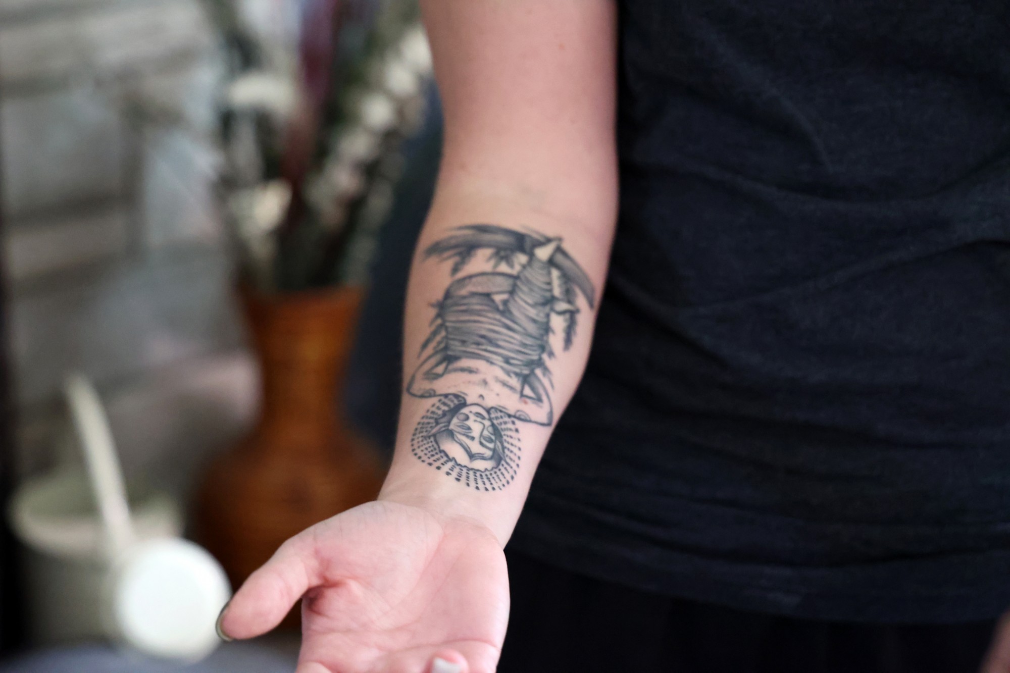 Image of Xan presenting the tattoo of The Hanged Man on their forearm.