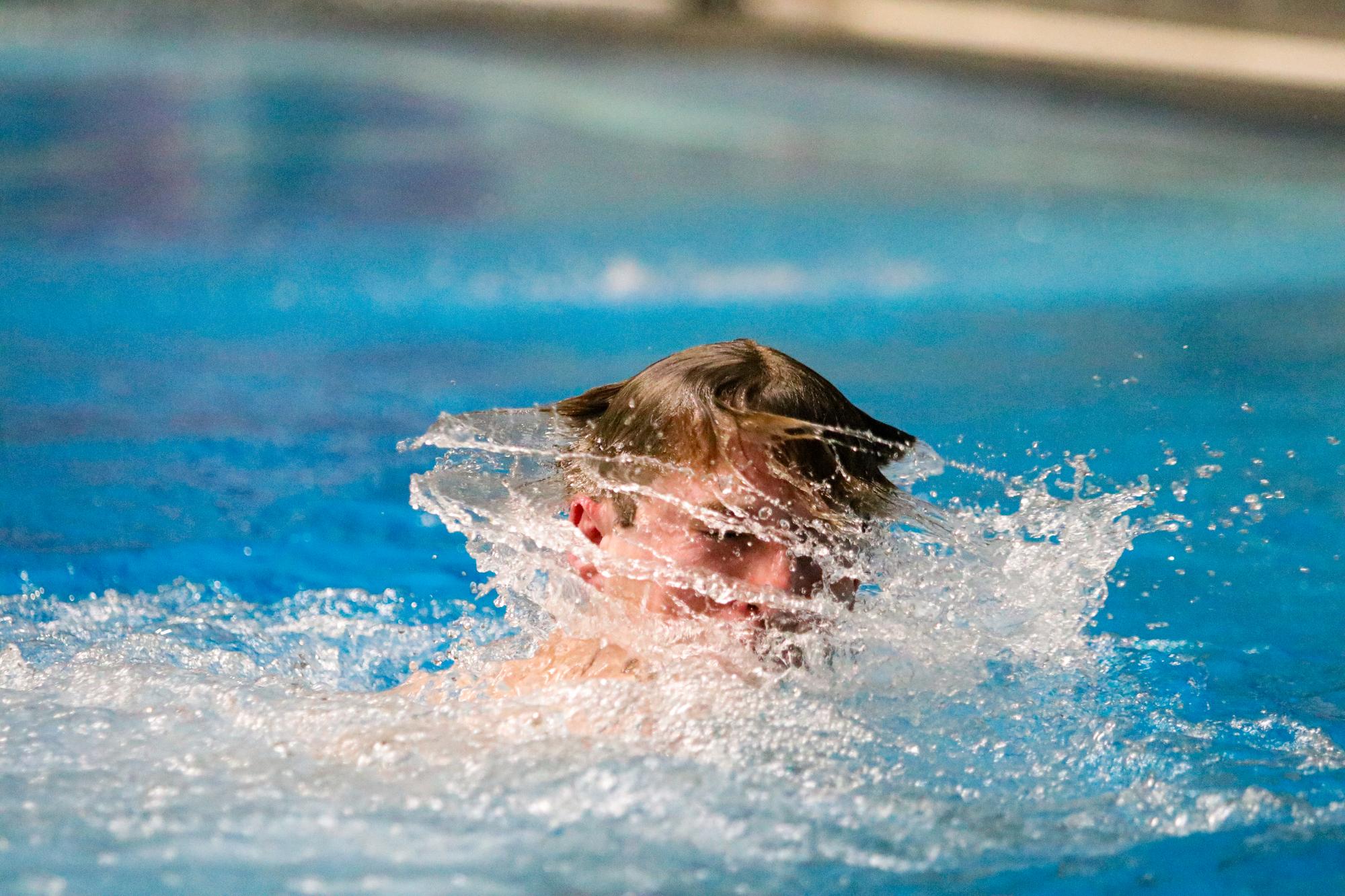 A diver emerges from the water and shakes water out of his hair.