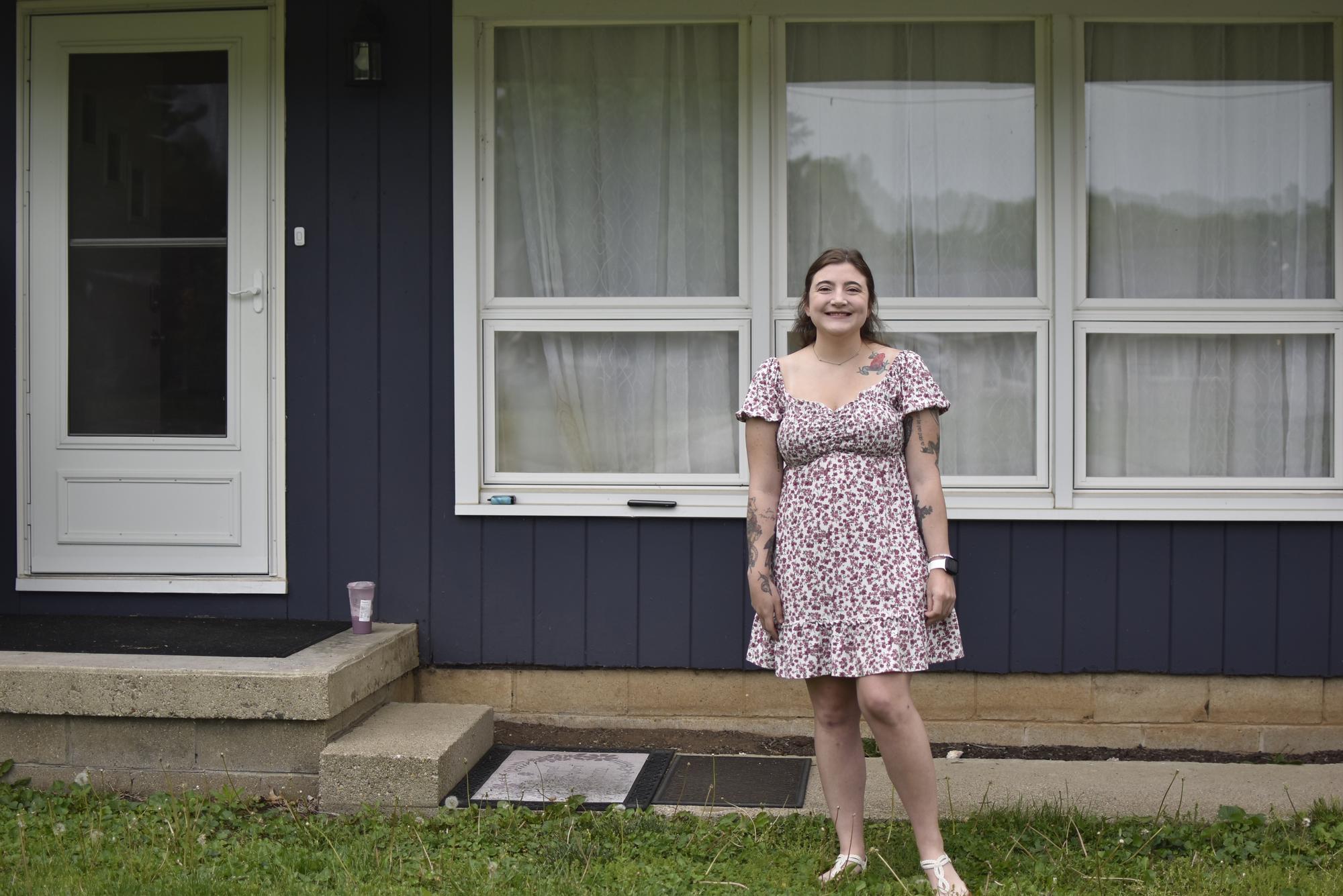 A woman poses in front of a window, wearing a flower print dress