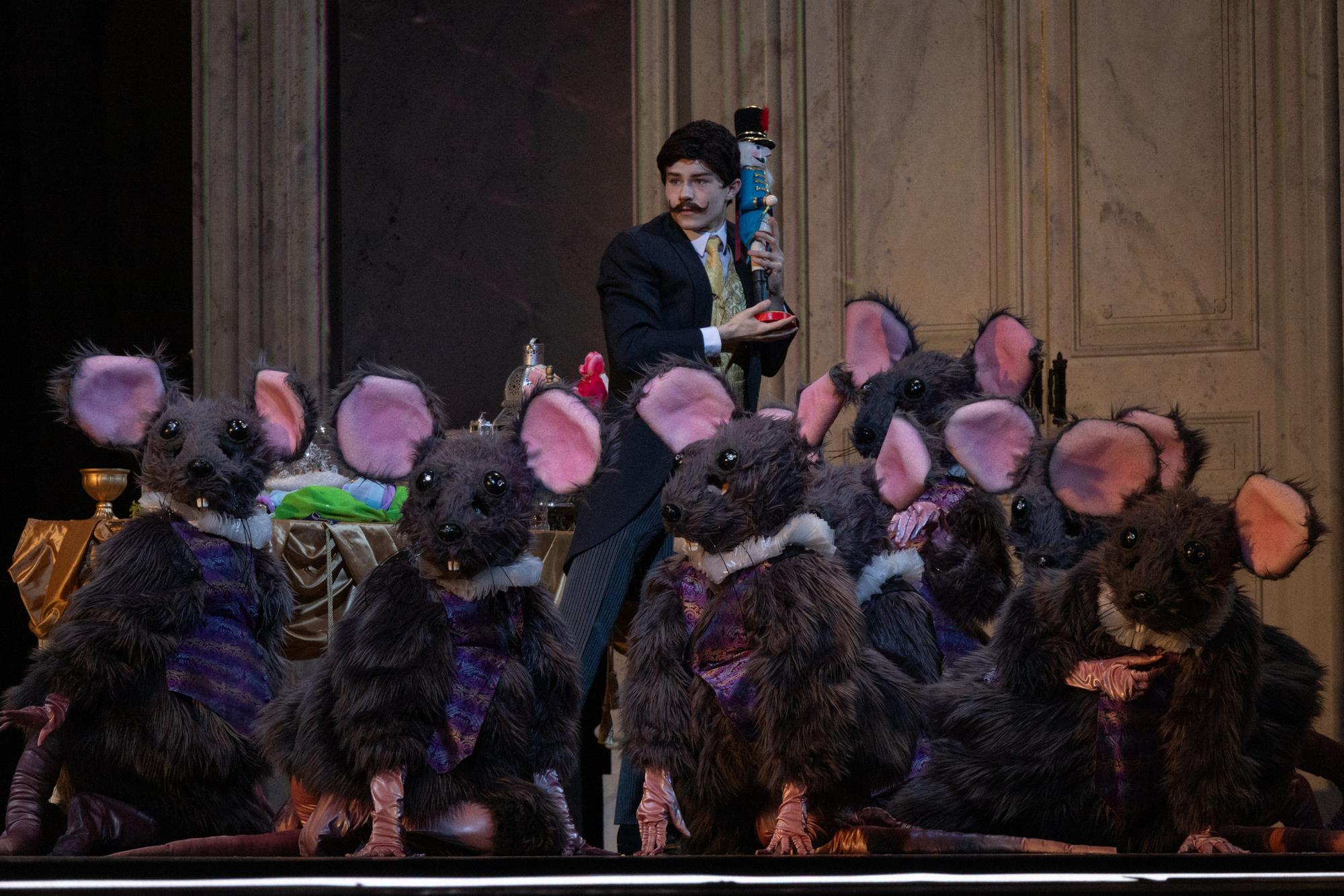 A mustachioed man suspiciously holds a doll while being swarmed by mice.