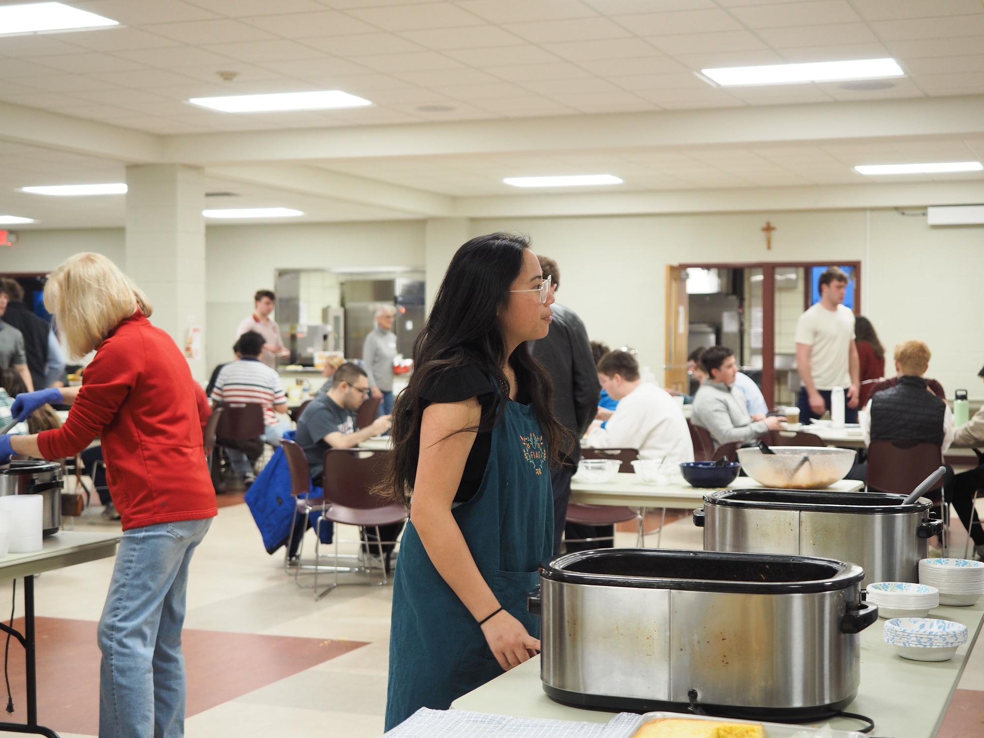 A student in a blue apron stands in front of a crockpot
