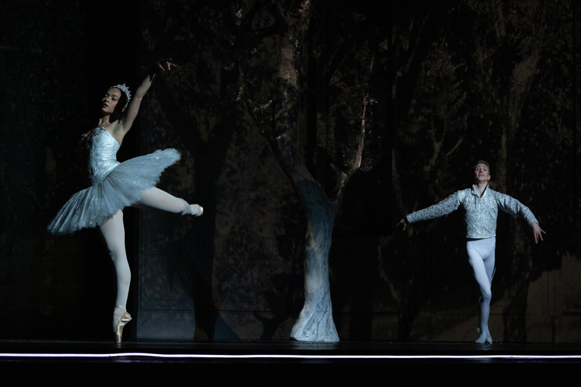 Two white clad dancers performing on a forested set.