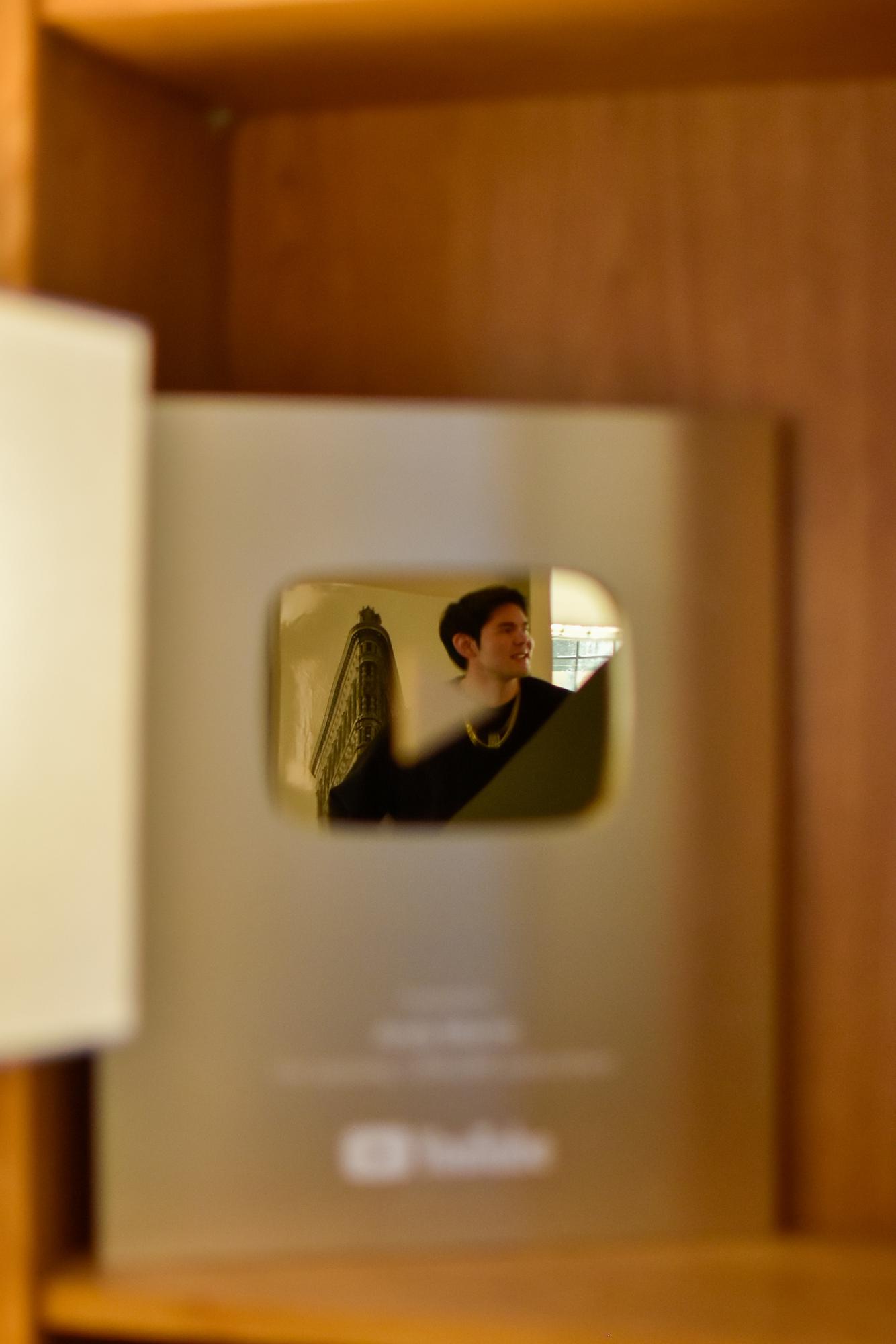 A person's face is reflected in a shiny gold play button