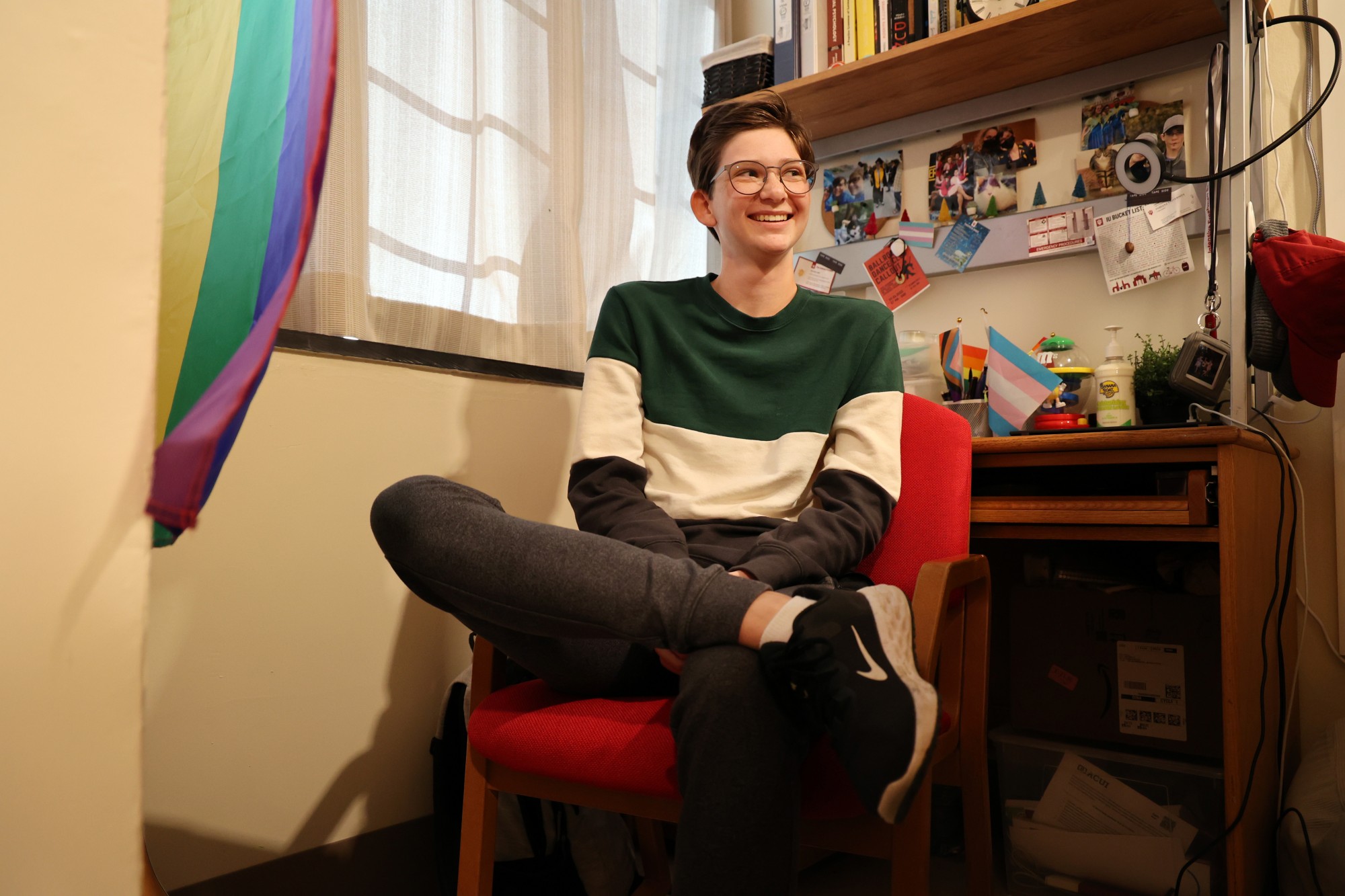 Photo of Elliot Wilson in their dorm. there is a Pride flag on the wall and a small trans flag on the desk. 