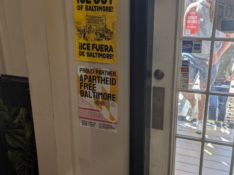 Photo from inside a store of their AFB poster. Above that poster is another poster which reads "ICE OUT OF BALTIMORE / ICE FUERA DE BALTIMORE"