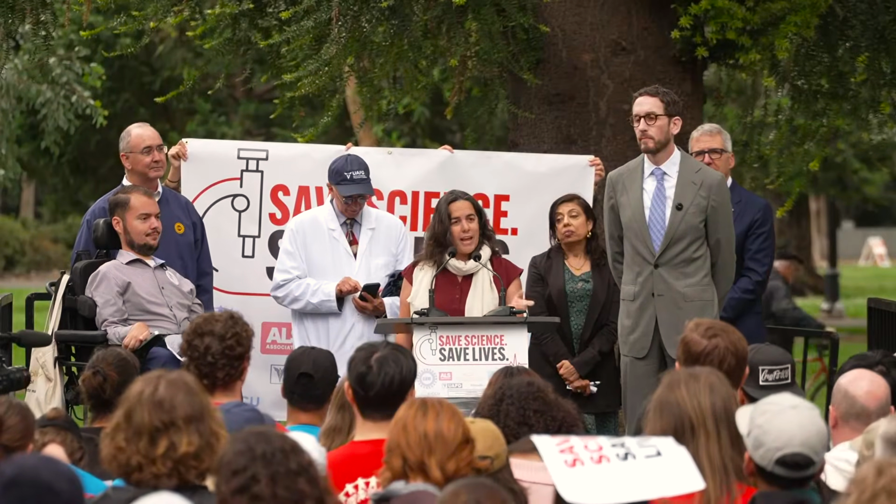 Professor Jessica Taft speaking on a podium in front of a large crowd with plackards and signs.