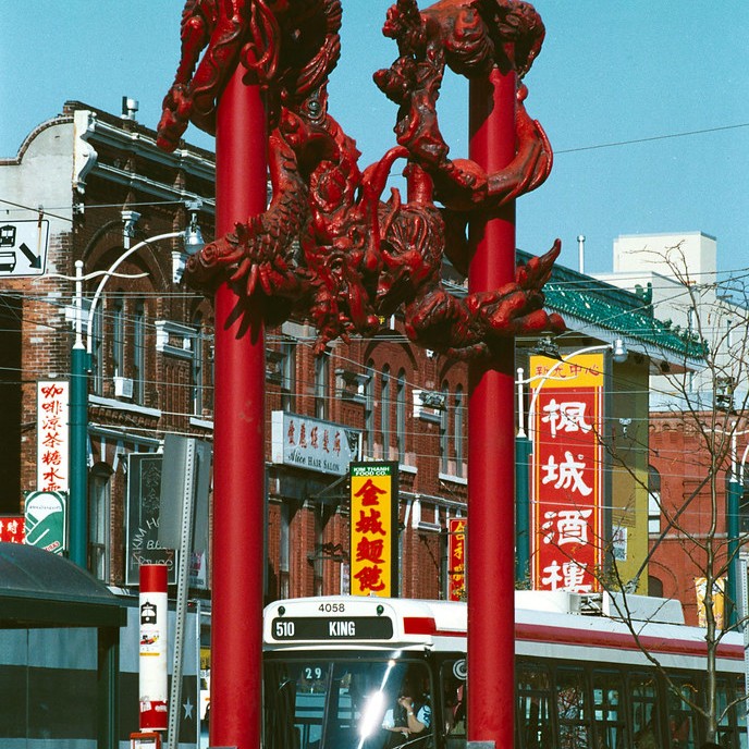 A photo of Toronto's Chinatown featuring the red dragon arch and an older streetcar