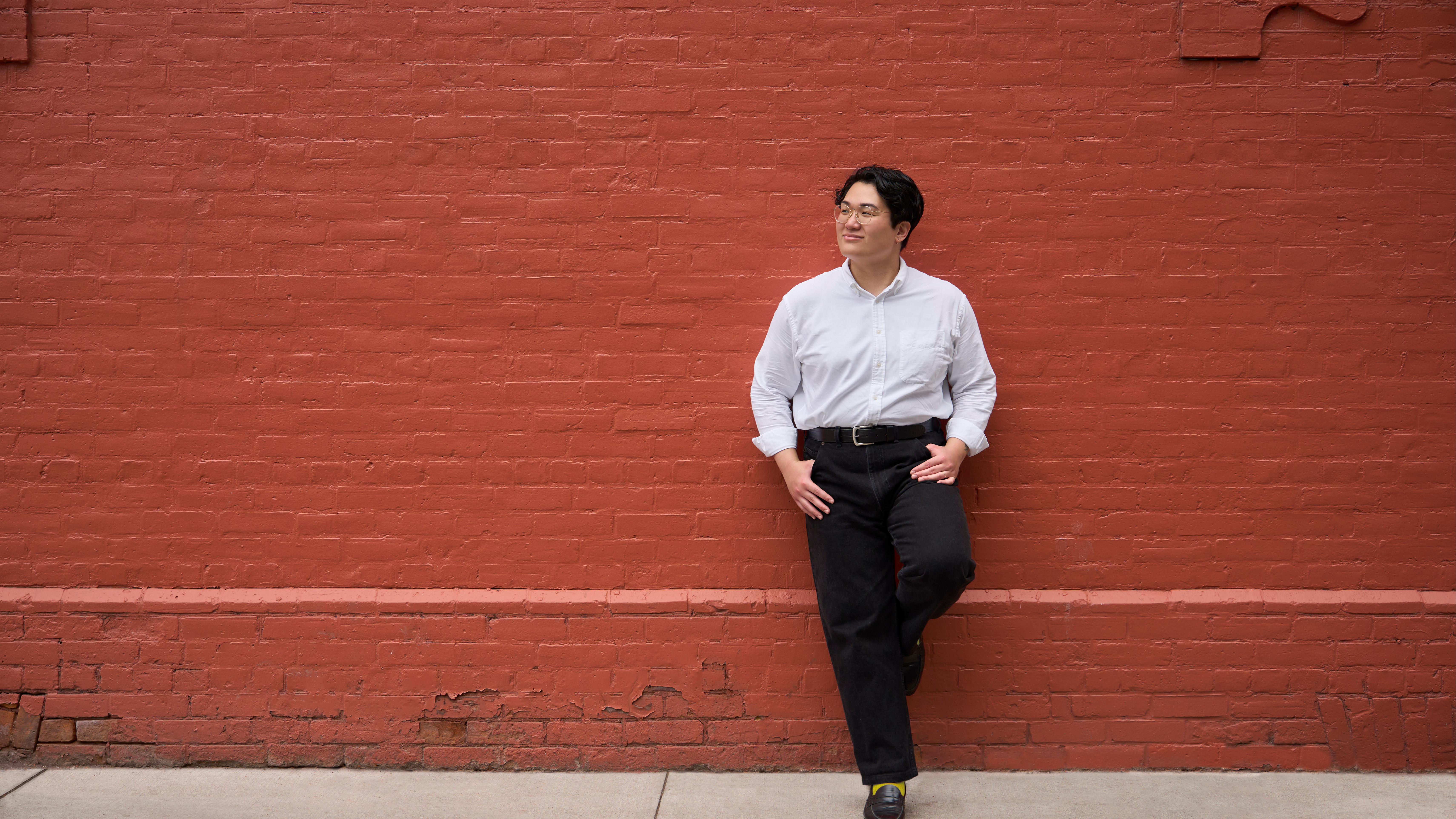 A photo of Andi, a non-binary Vietnamese person, leaning against a brick wall